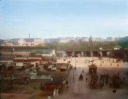 Der Matzleinsdorferplatz in Margareten. Im Hintergrund der querende Margaretengürtel, die Viadukte der Südbahn und der Protestantische Friedhof. Wien V. Handkoloriertes Glasdiapositiv. Um 1910.