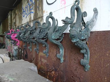Diese Metallelemente mit ihren Schwanenhälsen und seitlichen Flügeln dienten ursprünglich als Unterstützung für die Ausleger der großen schweren Laternen auf der alten Hauptbrücke.