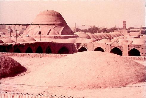 Das Zentrum der Oasenstadt Kerman im Iran verfügte noch 1973 über eine ungestörte Kuppeldachlandschaft. Alle Dächer sind aus Lehmziegeln und ohne Unterkonstruktion errichtet. Die grosse Kuppel links im Bild kennzeichnet einen Kreuzungspunkt im Bazar unterhalb.