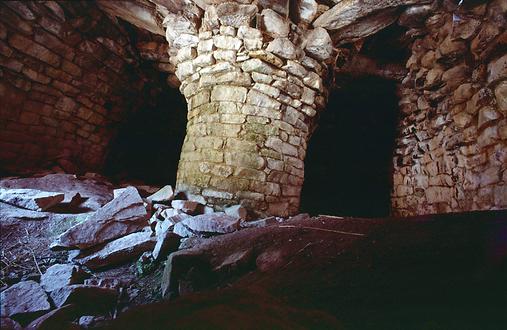Der Innenraum eines noch intakten Steinhauses mit runder Stütze im Zentrum und rundem Kraggewölbe.