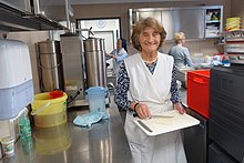 Frau mit weißer Schürze bereitet Tablett in der Großküche