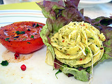 Foto von Kräuterbutter in Rosettenform auf Salat, daneben eine halbierte Tomate