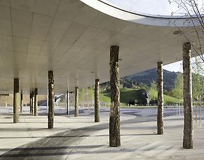 Eingangsgebäude; von Innsbrucker Architekturbüro s_o_s architekten; auf Birkenstämmen ruhendes weit ausladendes Dach als Schwelle zum Garten und zum vorgelagerten Großen Platz