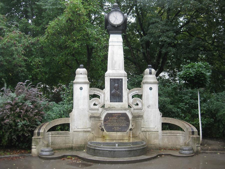 Arthaberbrunnen mit Uhr, Portrait und Rudolf von Arthaber-Widmungs- und Gedenktafel