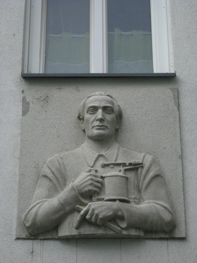 Hauszeichen als Kunststeinrelief 'Installateur' von Hugo Kirsch 1952