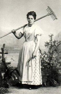 Portrait einer Frau im Dirndl mit Sichel und Rechen