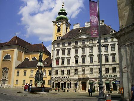 'Schubladkastenhaus', Freyung 7; Wien-Innere Stadt. Es war einmal das ehemalige Prioratshaus des (links anliegenden) Schottenstiftes. Auf dem Grund des 1751 aufgelassenen Klosterfriedhofes. Der Architekt hieß Andreas Zach und errichtete das Wohnhaus 1773/74 als 'schotttisches Freihaus auf dem Voglsang'. Die Wienerinnen und Wiener sahen im wichtigen Beispiel für die Wohnhausarchitektur des Barockklassizismus eher eine überdimensionierte Kommode, daher der Name Schubladkastenhaus. Vorne der Austria-Brunnen von Ludwig Schwanthaler (1846). Links die Klosterkirche des Schottenstiftes (15. Juni 2008 11:53:26) - Foto: Ernst Zentner