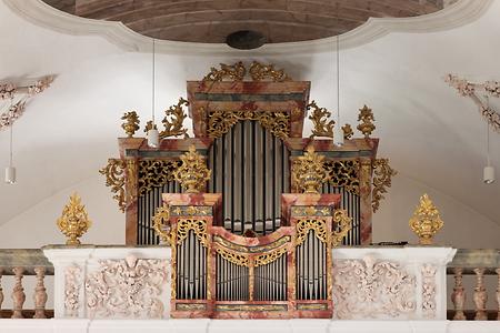 Orgel der Pfarrkirche Axams - Foto: Simon Legner (Simon04) (15. September 2022, 11:58:38) Wikimedia Commons - Gemeinfrei - Der Orgelbauer Johann König von Rattenberg stellte 1737 eine Orgel mit 16 Register fertig. 1831 umgebaut. Unter dem Organisten und Chorleiter Franz Apperl wurde 1908 eine neue sowie überarbeitete pneumatische Orgel der Orgelbaufirma Franz Reinisch II. konstruiert. Geringer Schaden durch kriegsbedingte Einschmelzung von Metallteilen 1944. Unter Verwendung originaler Bestandteile durch die österreichische Firma Orgelbau Pirchner aus Steinach am Brenner Neubau 1975 als mechanische Orgelwerk mit 17 Registern (zwei Manuale und Pedal). Das Orgelbauunternehmen begann mit der Herstellung von Orgel schon 1817. Die erwähnte Firma gibt es seit 2016 nicht mehr. Das Gotteshaus ist im Barockstil verwirklicht und enthält Fresken im Stil des Klassizismus und der Nazarener
