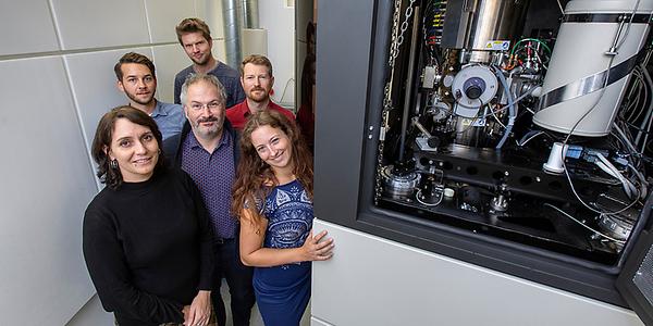 Eine Forschenden-Gruppe steht links neben dem Austrian Scanning Transmission Electron Microscope.