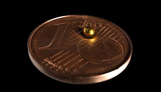 Die verwendete Goldkugel im Größenvergleich mit einer 1-Cent-Münze. Laut Einsteins Allgemeiner Relativitätstheorie krümmt jede Masse die Raumzeit