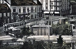 Abfahrtsstelle der Vöslauer Linie am Josefsplatz, links ein aus Wien angekommener Zug der Badner Bahn, davor wartend ein grün-créme lackierter Wagen der Serie 92–99.