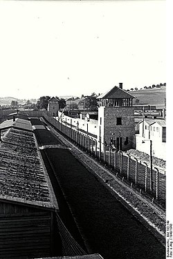 Steinerne Wachtürme, steinerne Mauer und Stacheldrahtzaun. Baracke im Vordergrund