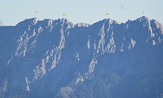 Hackenköpfe von Nordwesten, links der Östliche Hackenkopf (ÖH), mittig der Mittlere Hackenkopf (MH), weiter rechts der Westliche Hackenkopf (WH) und ganz rechts der Scheffauer (S), links von ihm der Widauersteig (Klettersteig)