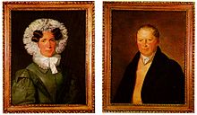 At left, a painted portrait of a woman in a black dress with a frilled hood and ruffled collar. At right, a painted portrait of a man in a black coat wearing a cravat.