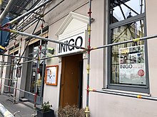 Altes Haus in Nahaufnahme mit einem Gerüst für Fassadenrenovierung davor. Über dem Eingangstor in der Mitte ist ein Schild mit der Aufrschrift "Inigo".