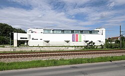 Ehemalige Essl Museum und jetziges Depot der Sammlung Essl in Klosterneuburg, direkt an Bahngleisen gelegen, ein gestreckter Baukörper in Weiß, der durch Fenstergalerie und weitere Farbakzente nur auf den ersten Blick ein Industriebau ist.