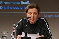 Frontansicht einer Frau mit zurückgebundenen Haaren an einem Tisch mit Mikrofon