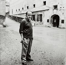 Giacomo Manzù steht auf einer regennassen Straße, Schwarzweißfotografie aus den frühen 1960er Jahren
