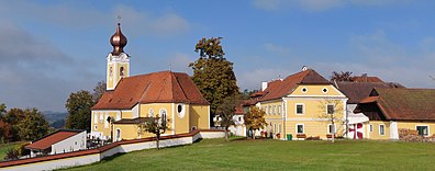 Spätbarocke Pfarrkirche mit Zwiebelturm, rotem Ziegeldach und gelbem Verputz; rechts daneben in gleicher Farbgebung der Pfarrhof mit Krüppelwalmdächern